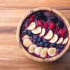acai berry smoothie in a wooden bowl topped with bananas, blueberries, raspberries and blackberries